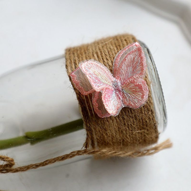 May include: A clear glass vase wrapped in brown twine with a pink and white butterfly embellishment.