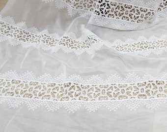 May include: White sheer fabric with a delicate white lace trim. The lace features a repeating geometric pattern.
