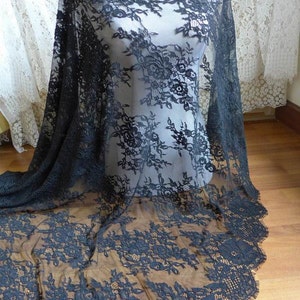 May include: Black floral lace fabric with a scalloped edge. The lace is delicate and sheer, with a floral pattern.