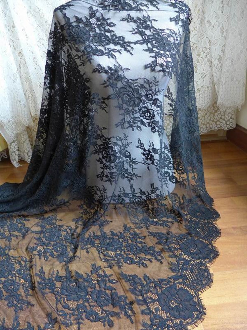 May include: Black floral lace fabric with a scalloped edge. The lace is delicate and sheer, with a floral pattern.