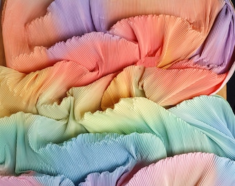 May include: A rainbow ombre pleated fabric with a soft, flowing texture. The fabric is folded in layers, creating a cascading effect of colors.