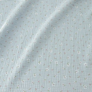 May include: Light blue fabric with a delicate floral pattern. The fabric features small white flowers with pink centers and green stems scattered across its surface. The fabric has a textured, crinkled appearance.