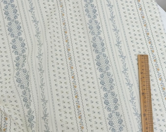 May include: Cream-colored fabric with a repeating floral pattern in blue and yellow. Vertical stripes alternate between solid and dotted lines. A wooden ruler is placed on the fabric, showing measurements in inches.