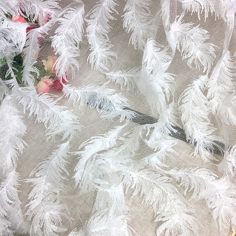 May include: White feather trim fabric with a delicate mesh background. The fabric features a repeating pattern of white feathers.