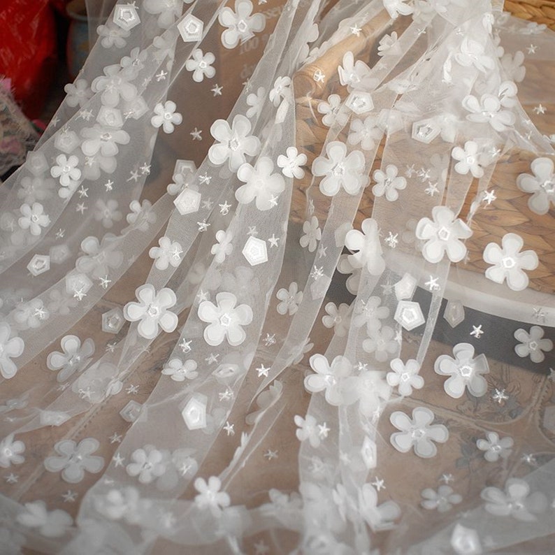 May include: White tulle fabric with 3D white flowers and stars. The fabric is sheer and delicate.