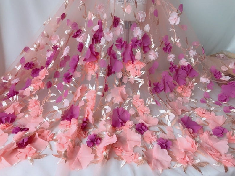 May include: Pink and purple 3D floral lace fabric with a delicate mesh background. The fabric features a gradient of colors, with pink flowers at the bottom and purple flowers at the top.