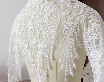 May include: White lace fabric with a floral design and fringe. The lace is delicate and intricate, with a scalloped edge.
