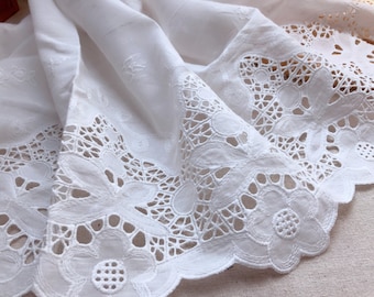 Könnte beinhalten: Weiße Baumwollspitzenborte mit einem gewellten Rand und filigranen Blumendesigns. Die Spitze hat eine zarte, luftige Haptik und wäre perfekt, um jedem Projekt einen Hauch von Eleganz zu verleihen.