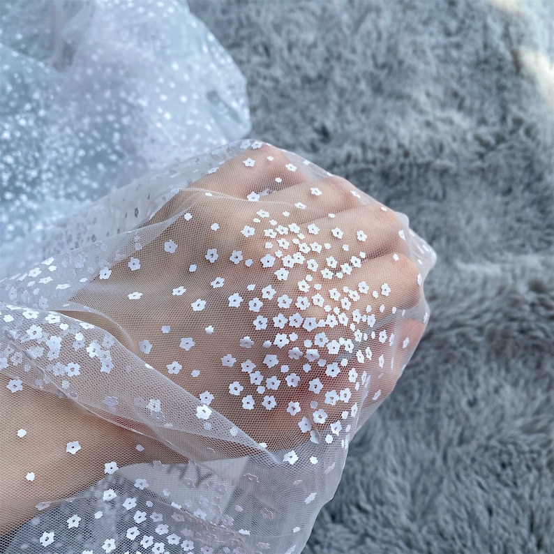 以下が含まれることがあります： 繊細な花柄の白い透き通った生地。生地は透き通っており、上品な輝きがあります。