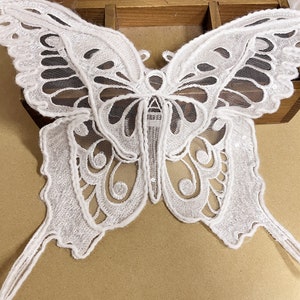 May include: White lace butterfly applique with a delicate design. The butterfly has a mesh center and intricate details around the edges.