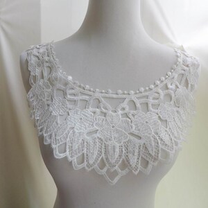 May include: White lace trim with a scalloped edge and floral design. The trim is approximately 5 inches wide.