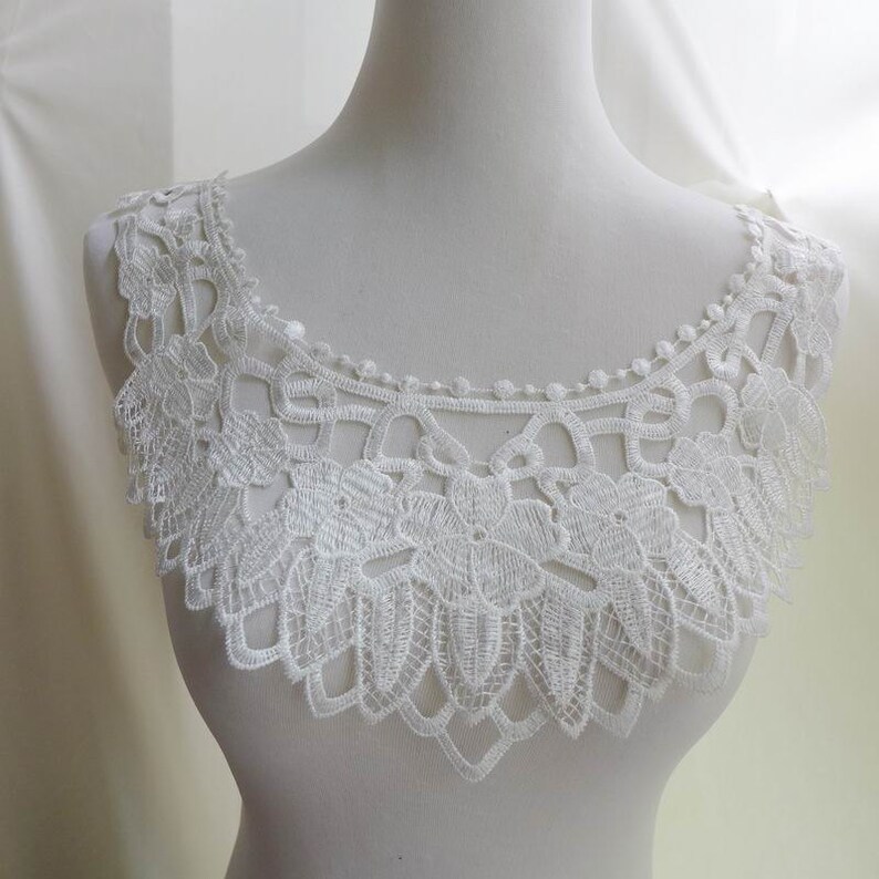 May include: White lace trim with a scalloped edge and floral design. The trim is approximately 5 inches wide.