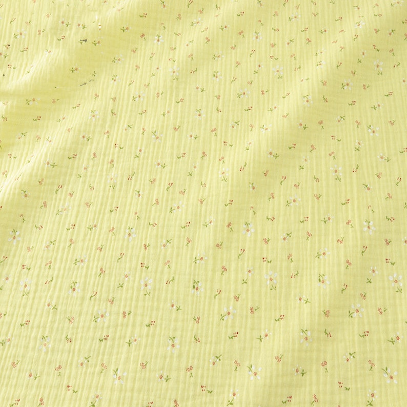 May include: A close-up of a yellow fabric with a floral pattern. The fabric has a textured, ribbed appearance. Tiny white and red flowers are scattered across the surface, creating a delicate, springtime aesthetic.