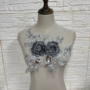 May include: A silver lace applique with two large grey satin flowers and silver sequins.