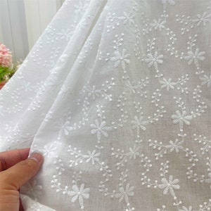 Puede incluir: Una tela blanca con un delicado patr&oacute;n bordado repetitivo de peque&ntilde;as flores y enredaderas. El bordado est&aacute; realizado con hilo blanco, creando una textura tonal sutil sobre el material ligero y semitransparente de la pieza.