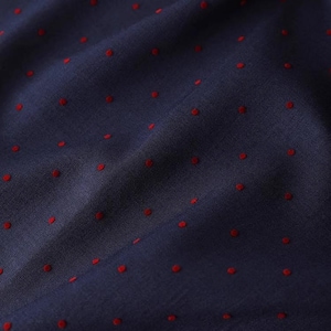May include: Close-up of a navy blue fabric with a pattern of small, evenly spaced red dots. The fabric is slightly textured and appears to be draped, with visible folds and shadows. The red dots are consistent in size and color.