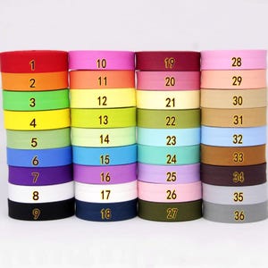 May include: Thirty-six rolls of colourful fabric ribbon, each with a number from 1 to 36 printed on it. The ribbon is arranged in rows of three, with each row containing a different colour.