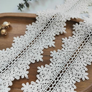 Op de afbeelding: Close-up van ivoorkanten afwerking met een bloemmotief. Het kant ligt op een houten dienblad. De afwerking heeft een geschulpte rand en is geschikt voor diverse knutselprojecten.