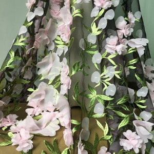 May include: Black mesh fabric with 3D pink and white flowers and green leaves. The fabric has a delicate and intricate design.