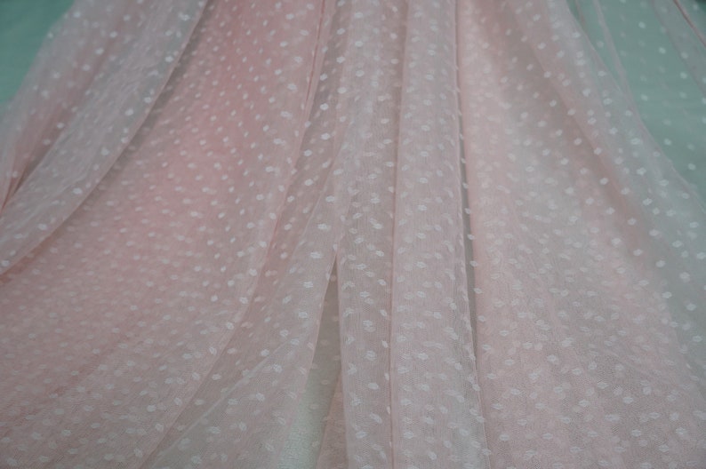 Puede incluir: Tela transparente rosa p&aacute;lido con un patr&oacute;n de lunares blancos. La tela est&aacute; doblada y drapeada, mostrando la textura y el patr&oacute;n.