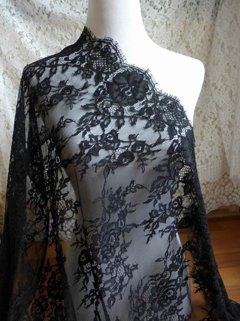 May include: Black lace fabric with a floral pattern. The lace has a scalloped edge.