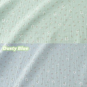 May include: Two sections of fabric, one light green and one dusty blue, are shown. Both fabrics have a crinkled texture and are covered in small white and pink floral patterns. The words "Light Green" and "Dusty Blue" are written above each fabric.
