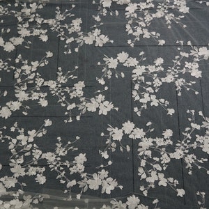 May include: White floral lace fabric with a delicate, embroidered design. The pattern features clusters of flowers and leaves, creating a romantic and elegant aesthetic. Ideal for bridal wear or decorative projects.