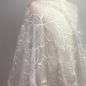 May include: White floral lace fabric with a delicate, intricate design. The lace is sheer and has a soft, flowing texture.