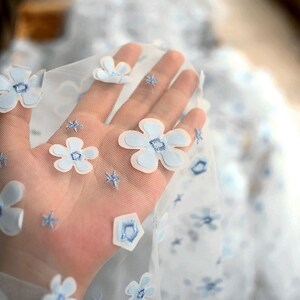 May include: Light blue sheer fabric with embroidered white and blue flowers. The fabric is delicate and has a soft, airy feel.