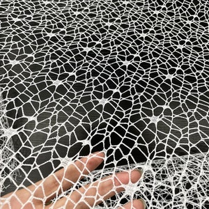 May include: White crochet fabric with a delicate spiderweb pattern. The fabric is soft and lightweight, making it ideal for crafting and decorating.