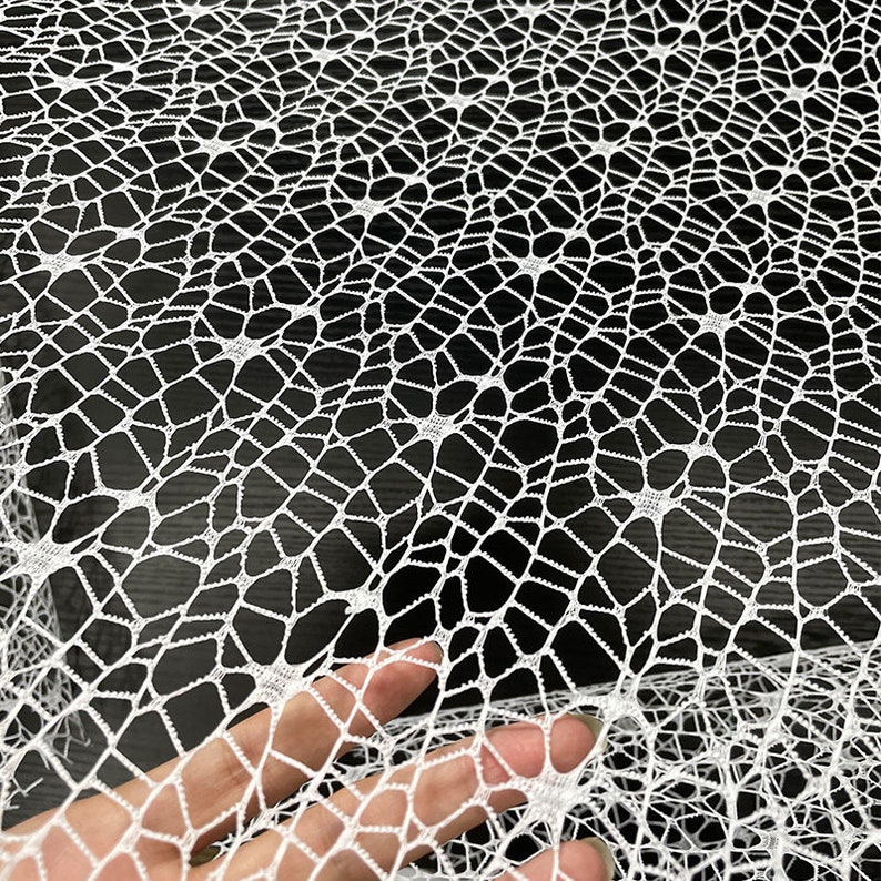 May include: White crochet fabric with a delicate spiderweb pattern. The fabric is soft and lightweight, making it ideal for crafting and decorating.