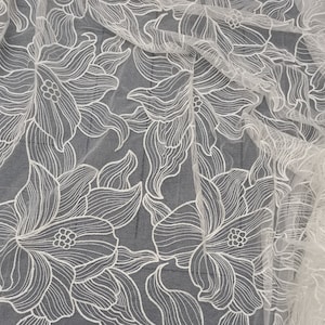 May include: White floral lace fabric with a delicate, intricate design. The fabric is sheer and lightweight, making it perfect for a variety of projects.