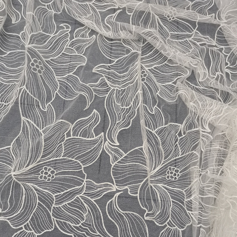 May include: White floral lace fabric with a delicate, intricate design. The fabric is sheer and lightweight, making it perfect for a variety of projects.