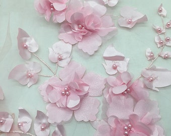 以下が含まれることがあります： ピンクの花柄レース生地に3Dの花とパールがあしらわれています。生地は繊細で透き通った質感で、どんなプロジェクトにもエレガントなアクセントを加えるのに最適です。