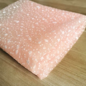 May include: Peach-colored tulle fabric with a white star pattern. The fabric is folded in half and has a soft, delicate texture.