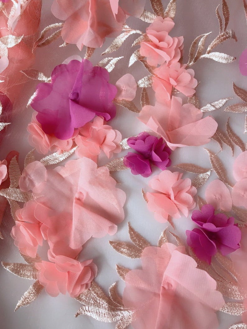 May include: Pink and purple 3D floral lace fabric with a delicate embroidered design. The fabric features a variety of flower shapes and sizes, with a soft, textured feel.