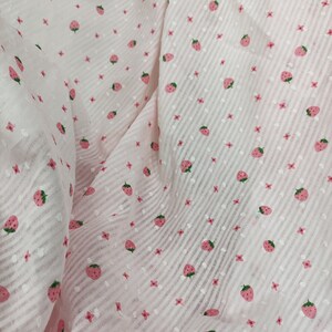 May include: Pink fabric with a white and pink striped pattern and a repeating strawberry print.