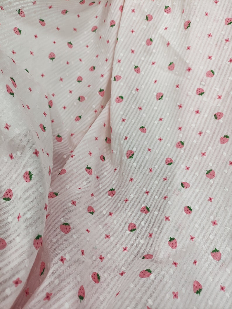 May include: Pink fabric with a white and pink striped pattern and a repeating strawberry print.