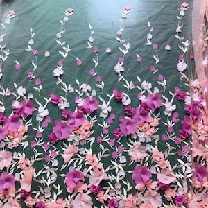 May include: Pink and purple 3D floral lace fabric with a delicate mesh background. The fabric features a repeating pattern of flowers and leaves.