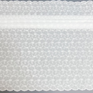 Puede incluir: Una tela blanca transparente con un intrincado patr&oacute;n bordado de peque&ntilde;as flores y delicadas enredaderas. El material tiene un borde festoneado en la parte superior e inferior, mostrando un motivo floral repetitivo en toda la superficie.