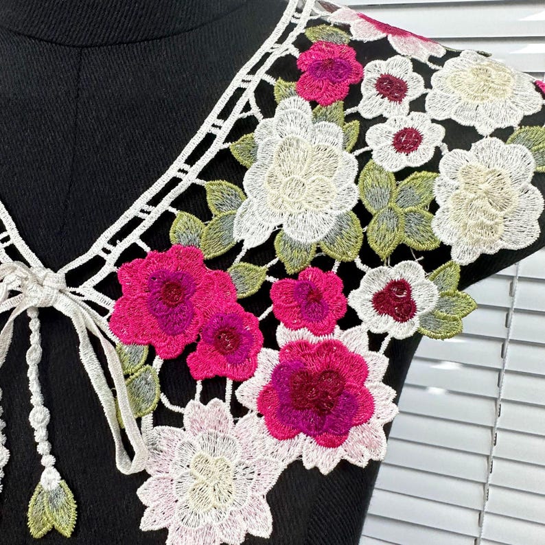 May include: White lace collar with pink and white floral embroidery. The collar has a tie fastening at the back.