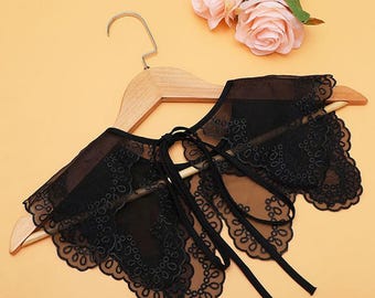 May include: Black lace collar with a delicate floral pattern. The collar is made of sheer fabric and has a tie closure at the back.