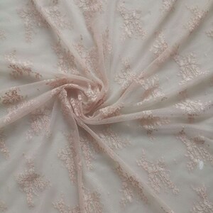 May include: Pale pink lace fabric with a delicate floral pattern. The fabric is sheer and has a soft, flowing texture.