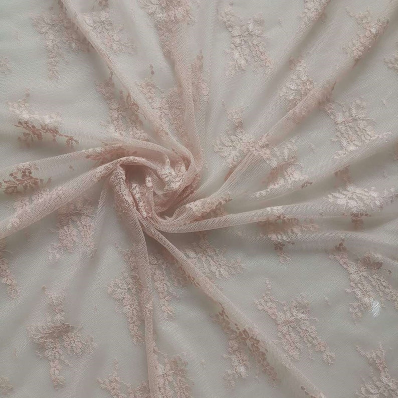May include: Pale pink lace fabric with a delicate floral pattern. The fabric is sheer and has a soft, flowing texture.