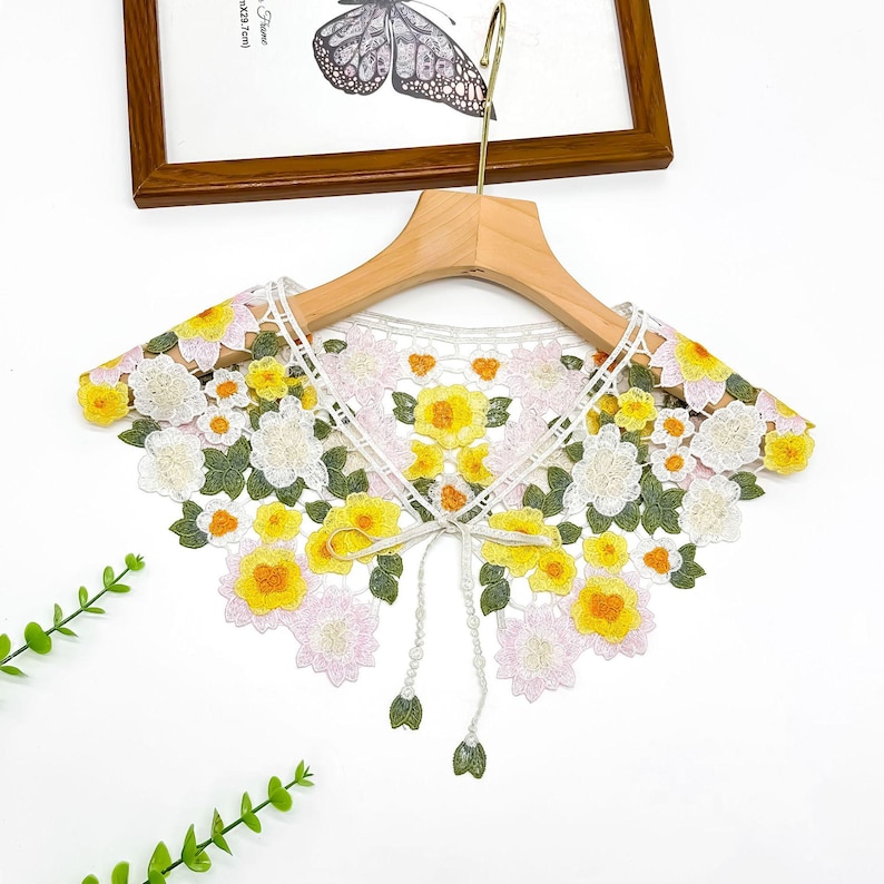 May include: White lace collar with yellow and pink floral embroidery. The collar has a tie fastening at the front.