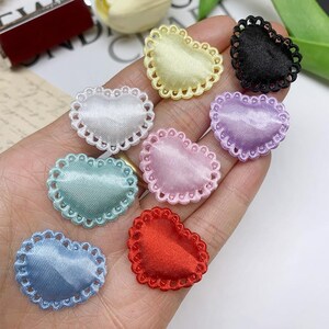 May include: Assortment of eight heart-shaped fabric embellishments with scalloped edges. The embellishments are in various colors, including red, pink, blue, green, white, yellow, purple, and black.