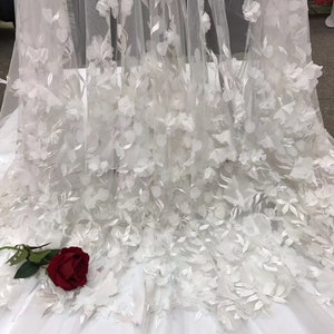 May include: White tulle fabric with 3D floral appliques. The fabric is delicate and sheer, with a soft, romantic feel. The flowers are raised and have a realistic appearance.