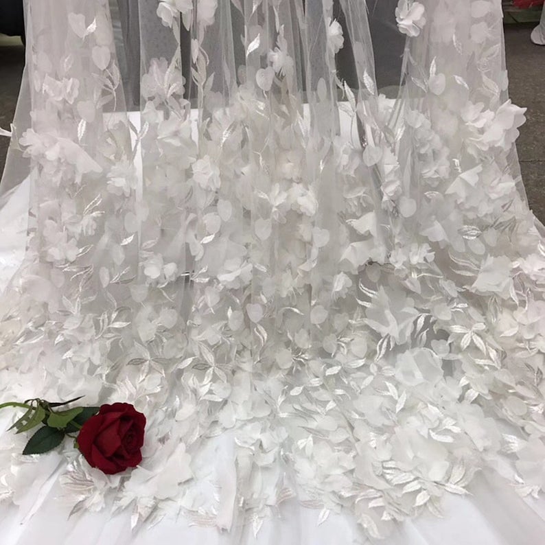May include: White tulle fabric with 3D floral appliques. The fabric is delicate and sheer, with a soft, romantic feel. The flowers are raised and have a realistic appearance.