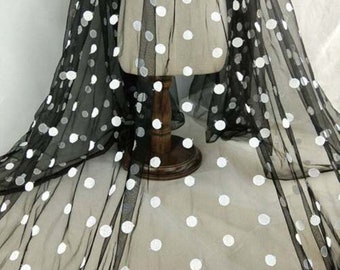 May include: Black sheer fabric with white polka dots. The fabric is draped over a mannequin form.