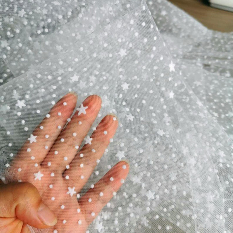 May include: White tulle fabric with a white polka dot and star pattern.